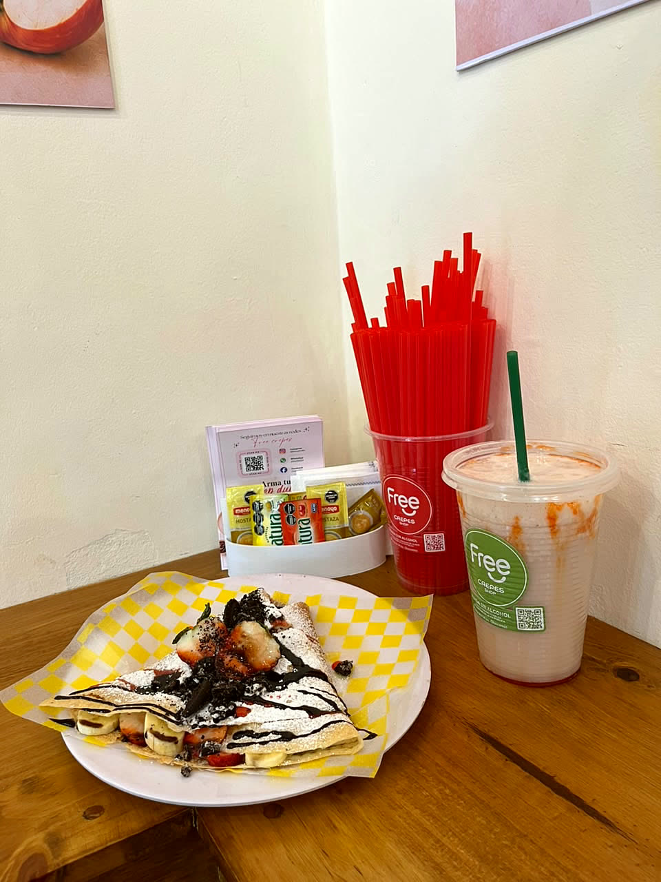 Crepe dulce con chocolate y frutilla junto a un licuado en vaso Free Crepes